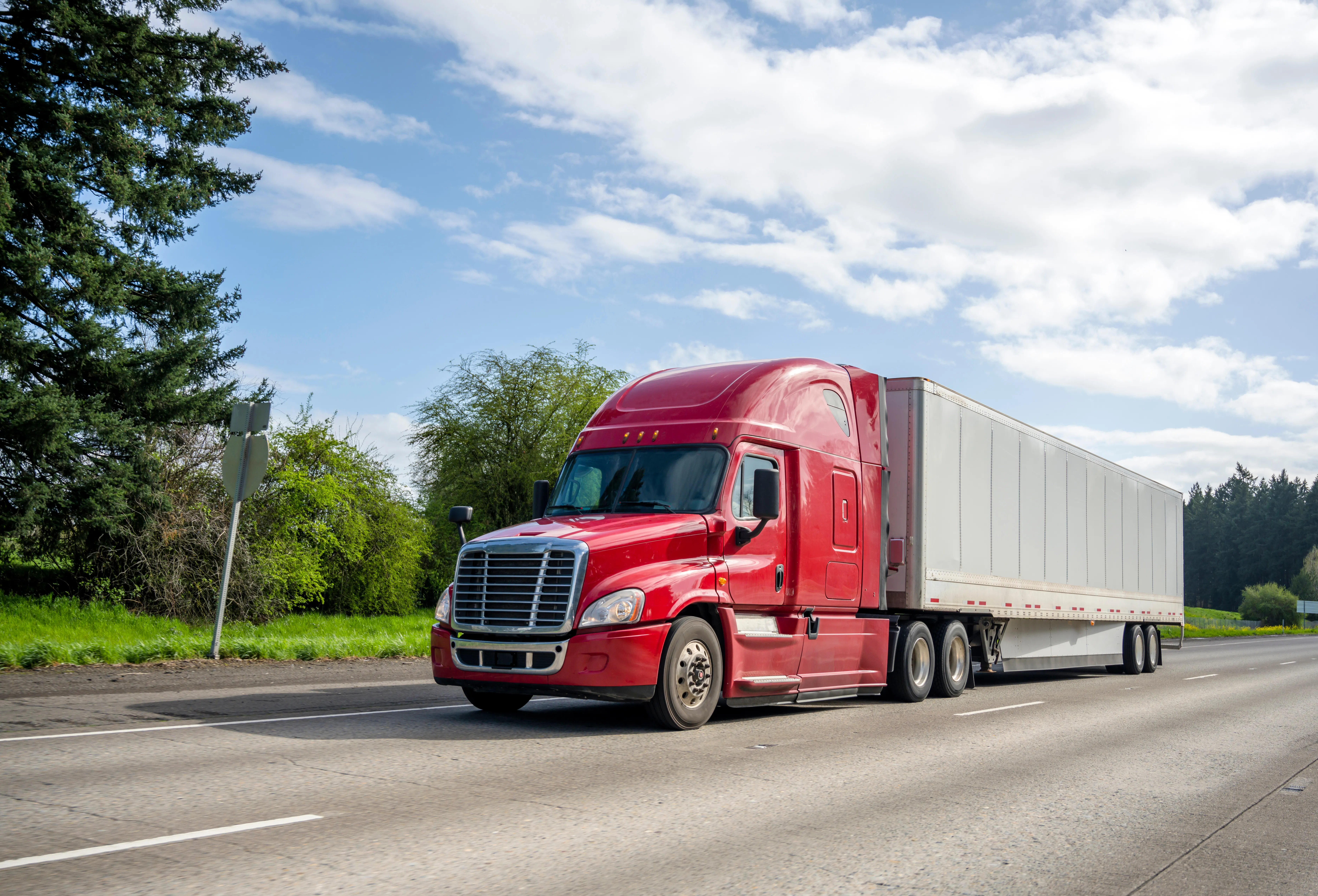 Red semi truck pulling a white dry van trailer on the highway