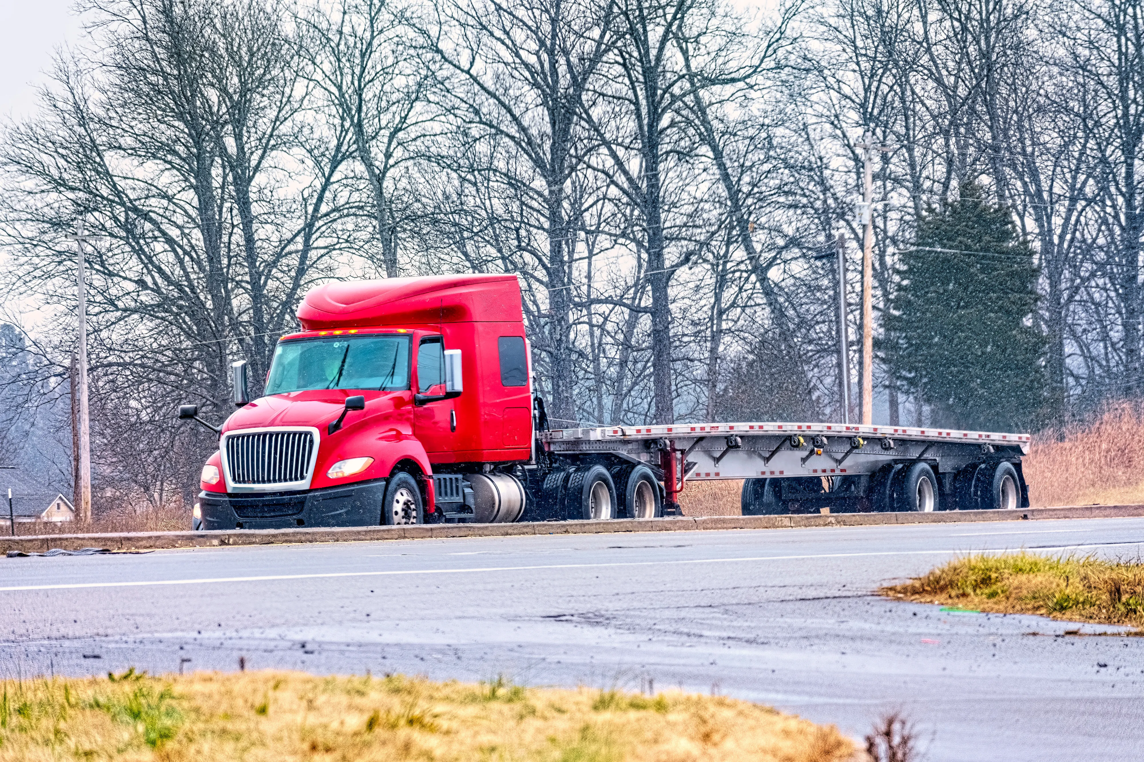Red semi truck with an empty flatbed trailer in winter weather