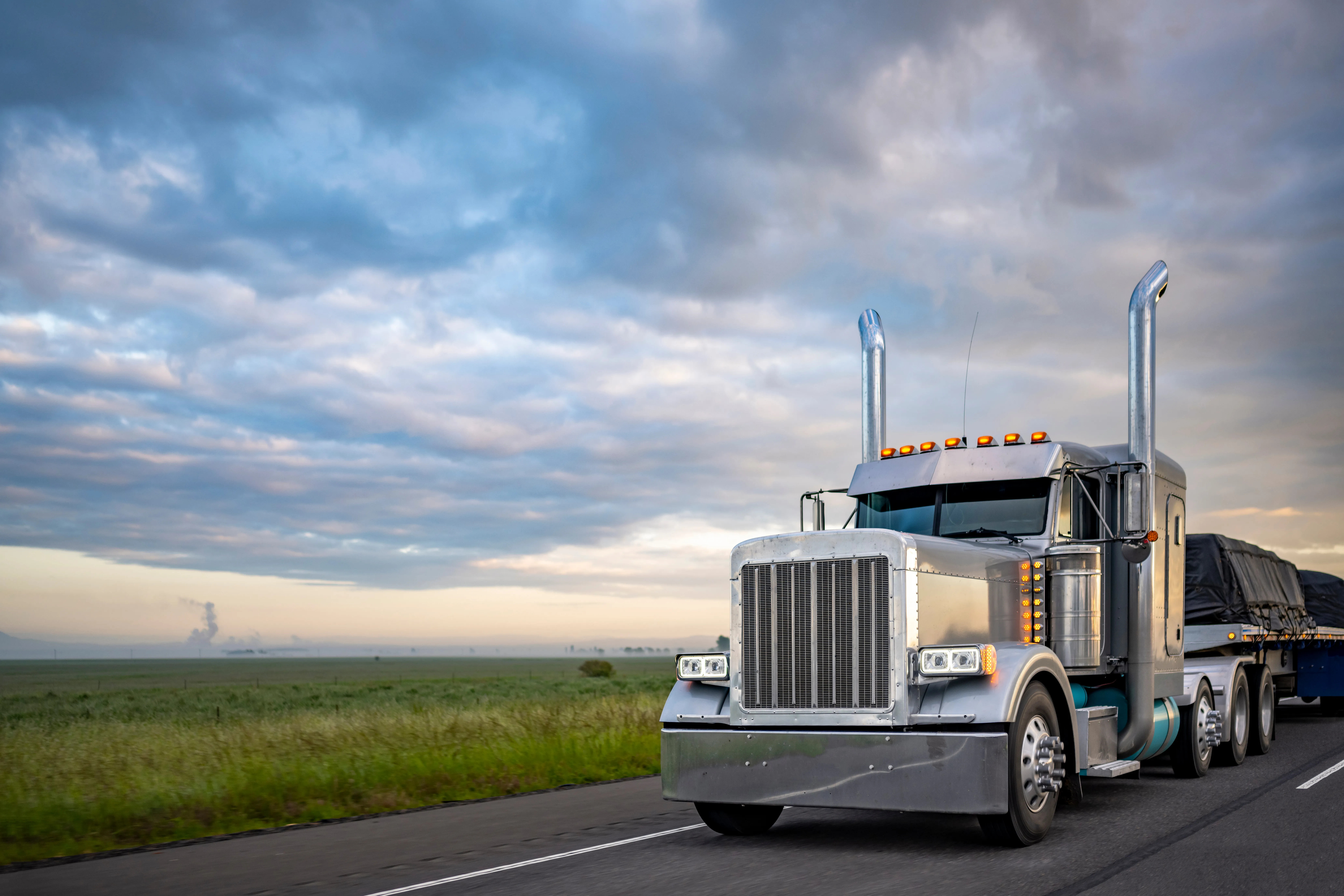 Chrome semi truck hauling a tarped flatbed load at dusk
