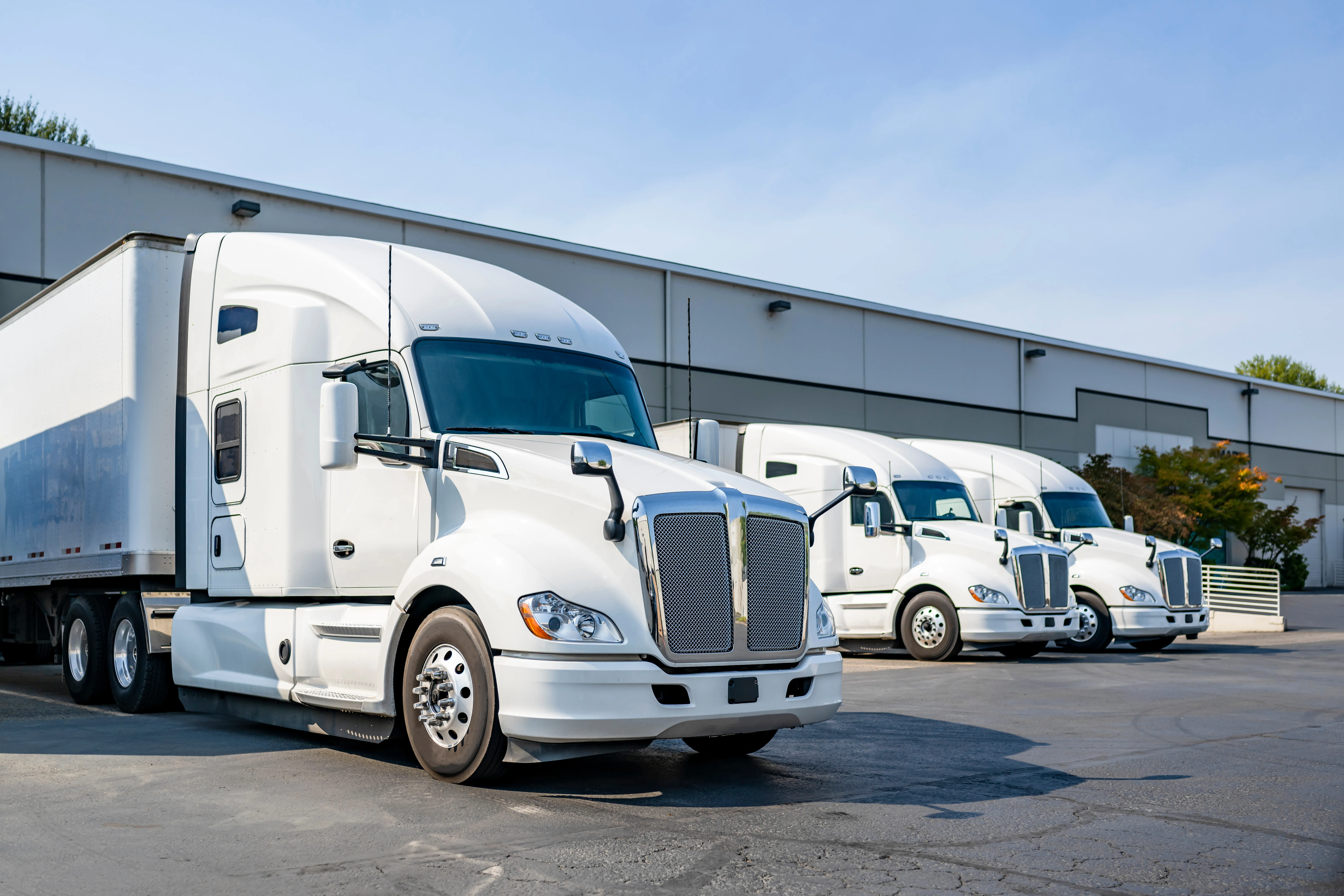 Row of white semi trucks parked at a distribution warehouse